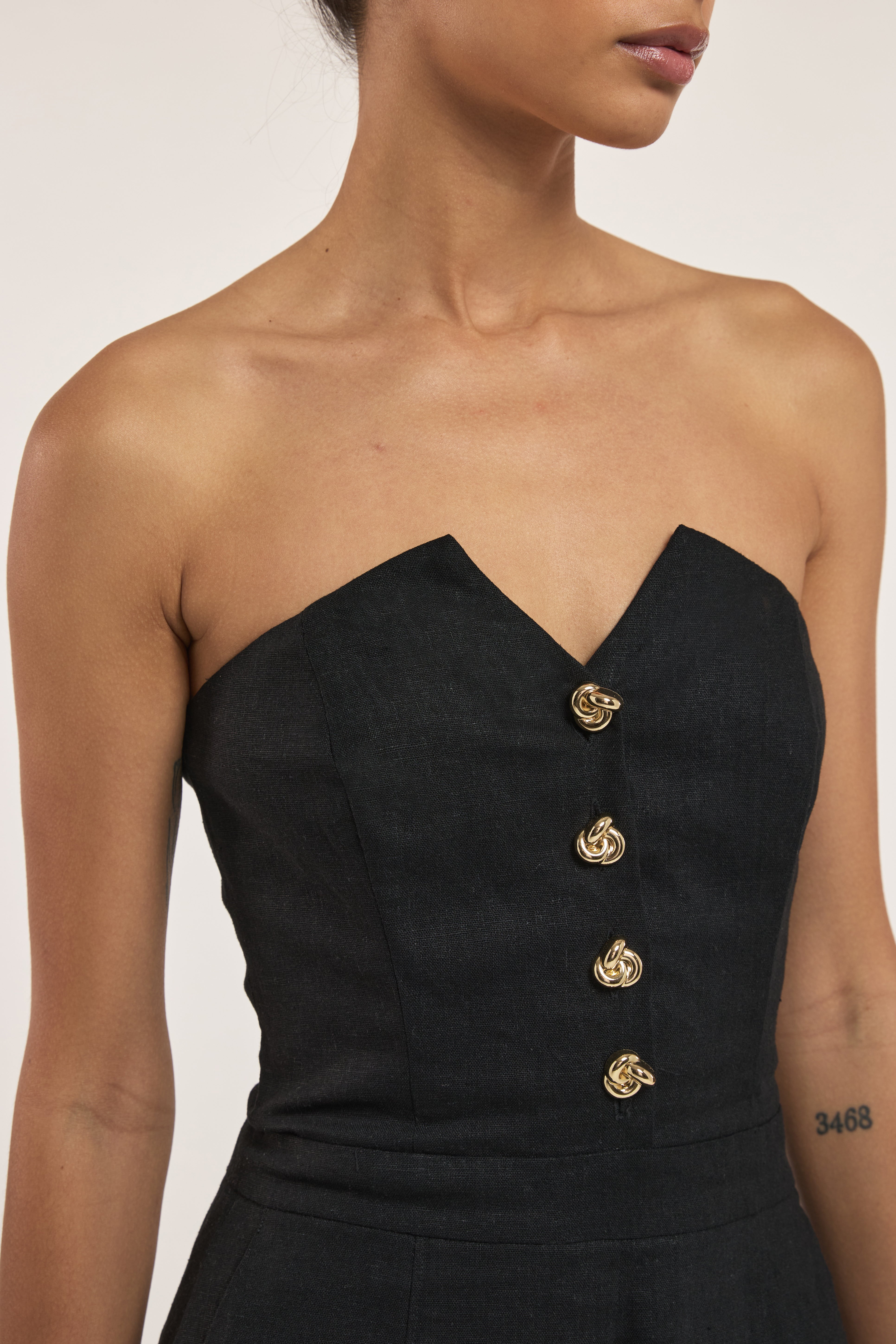 Black strapless romper with gold buttons on a neutral background