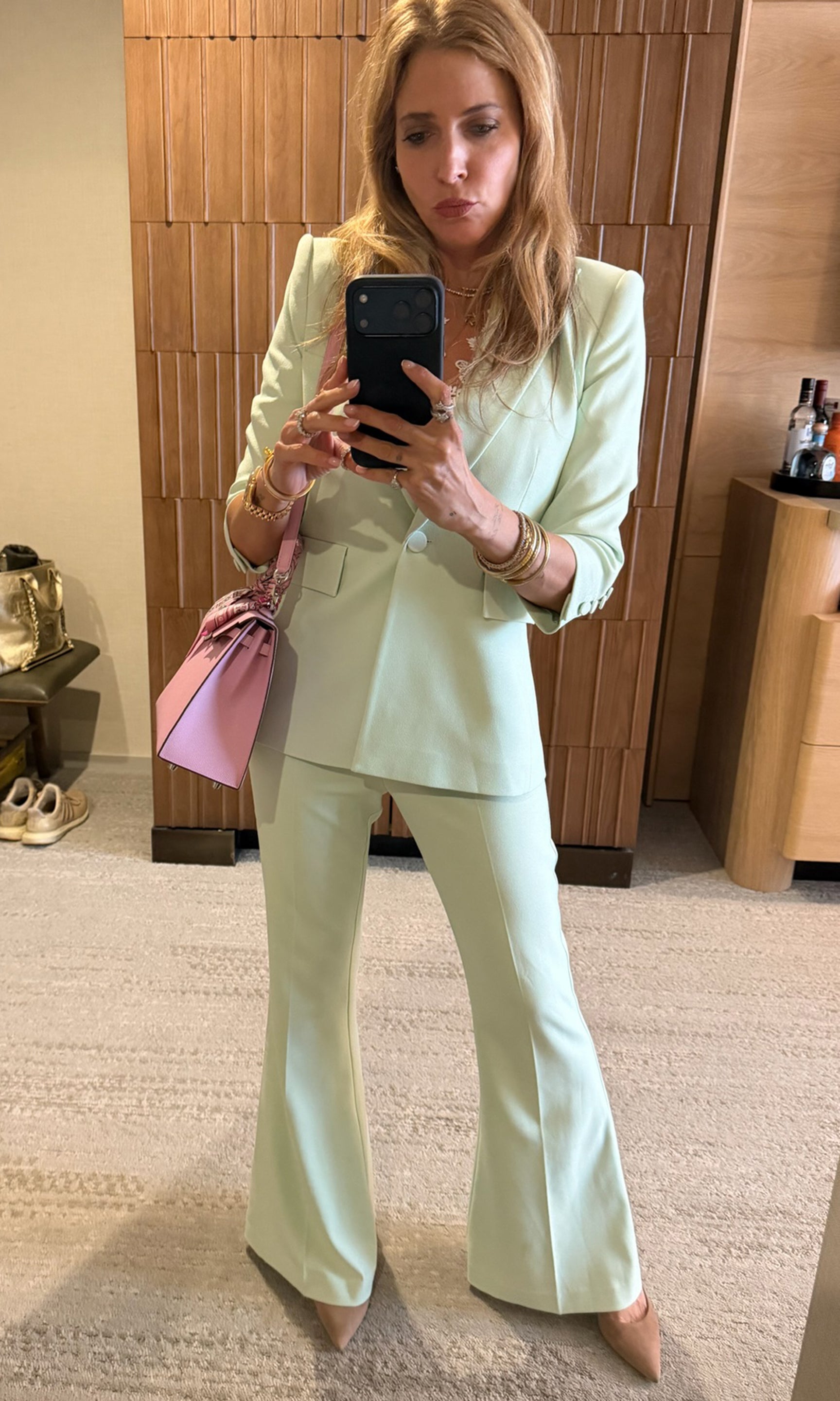 Founder Roni in a light green suit taking a mirror selfie in a room with wooden paneling.