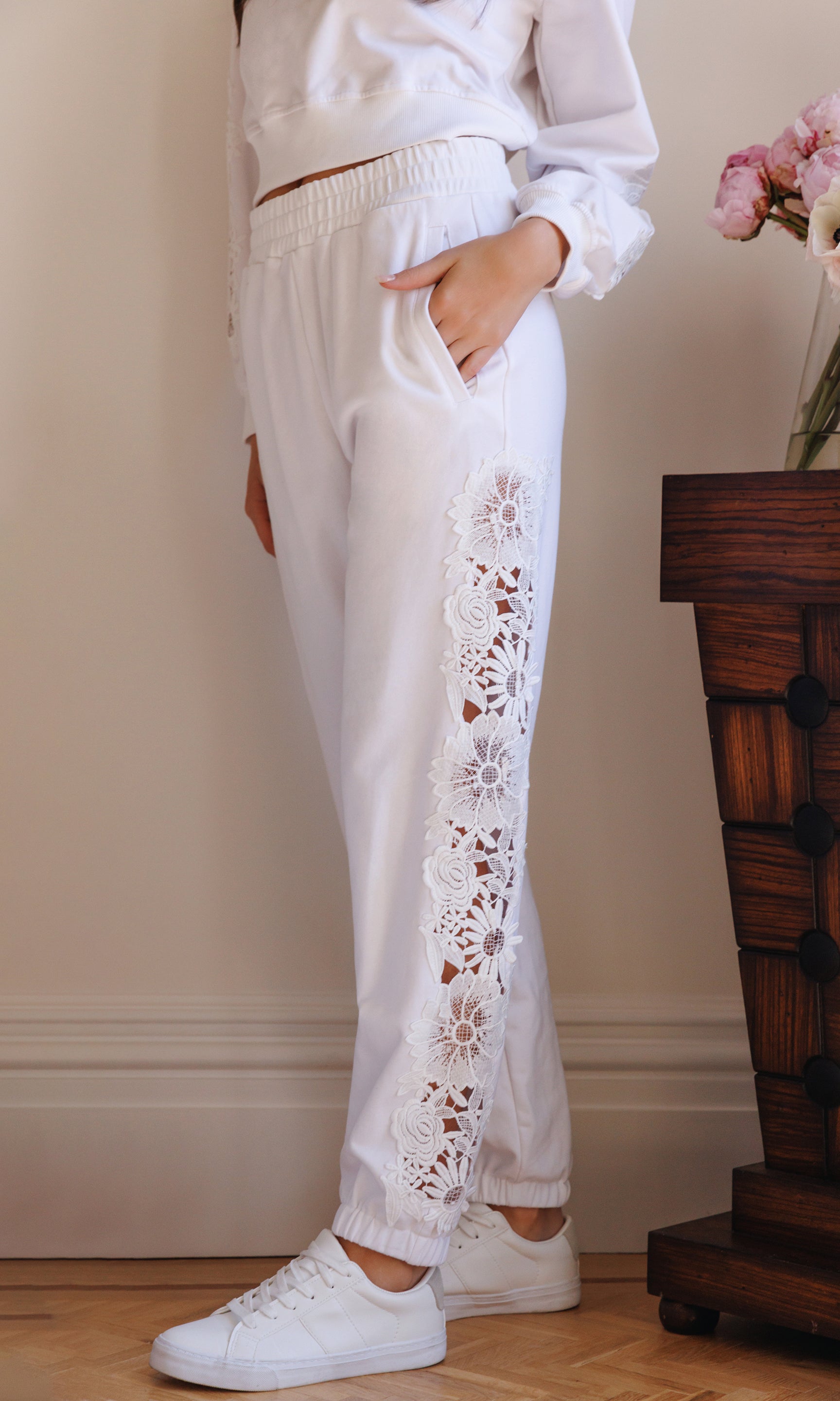 The model wears the Winnie Lace Combo Jogger in white in a side view, highlighting the relaxed jogger fit and the lace panel detailing running down the leg.