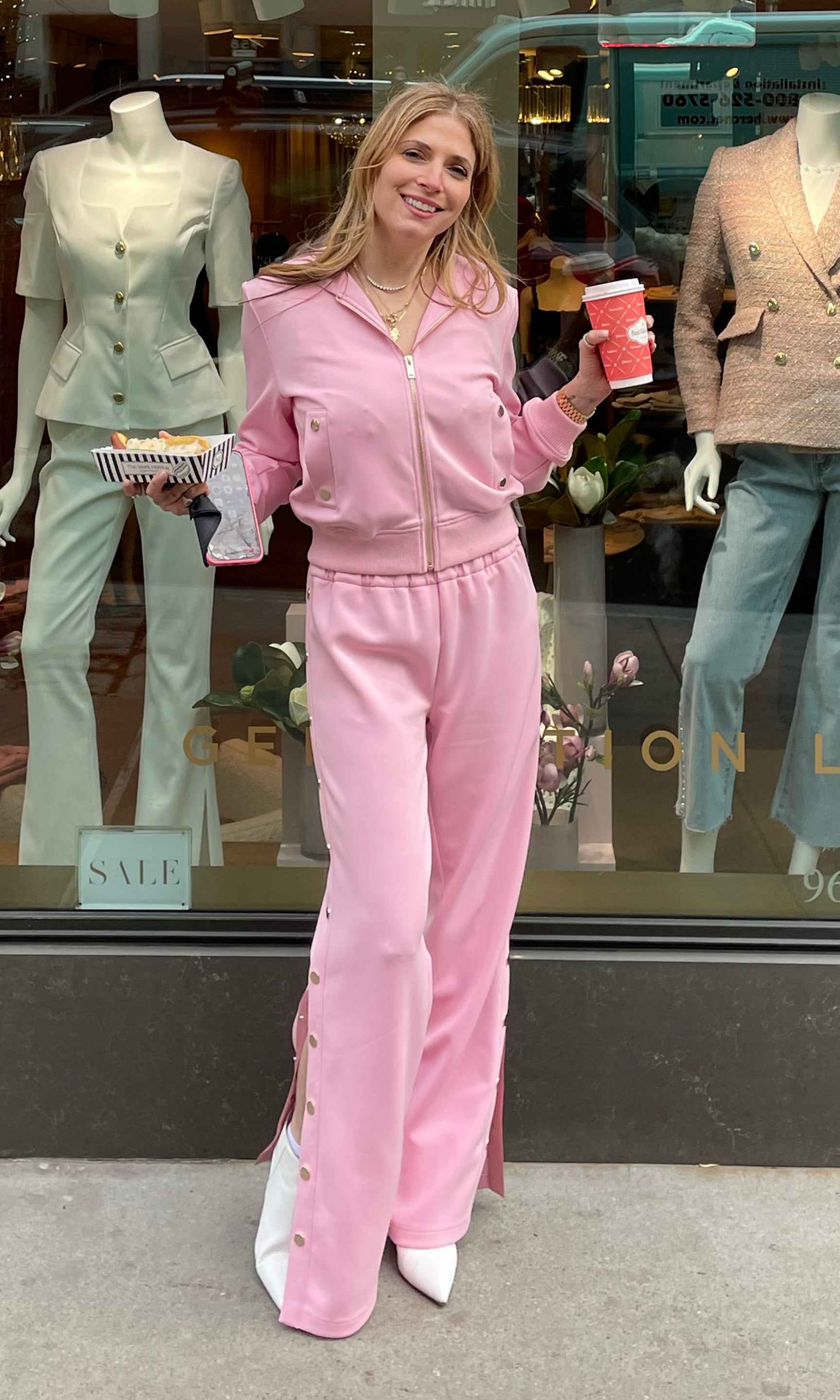 Founder Roni in a pink outfit holding a coffee cup in front of a store window display.