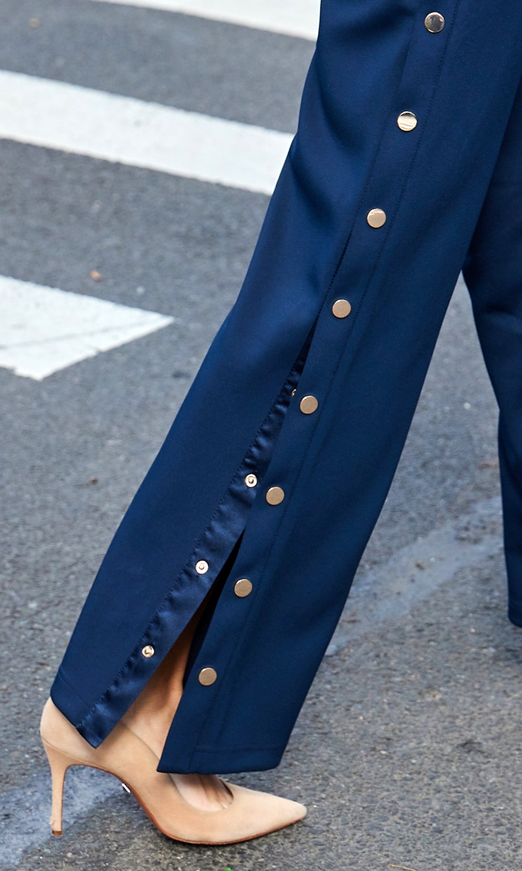 Navy blue pants with gold buttons worn by a person on a street.