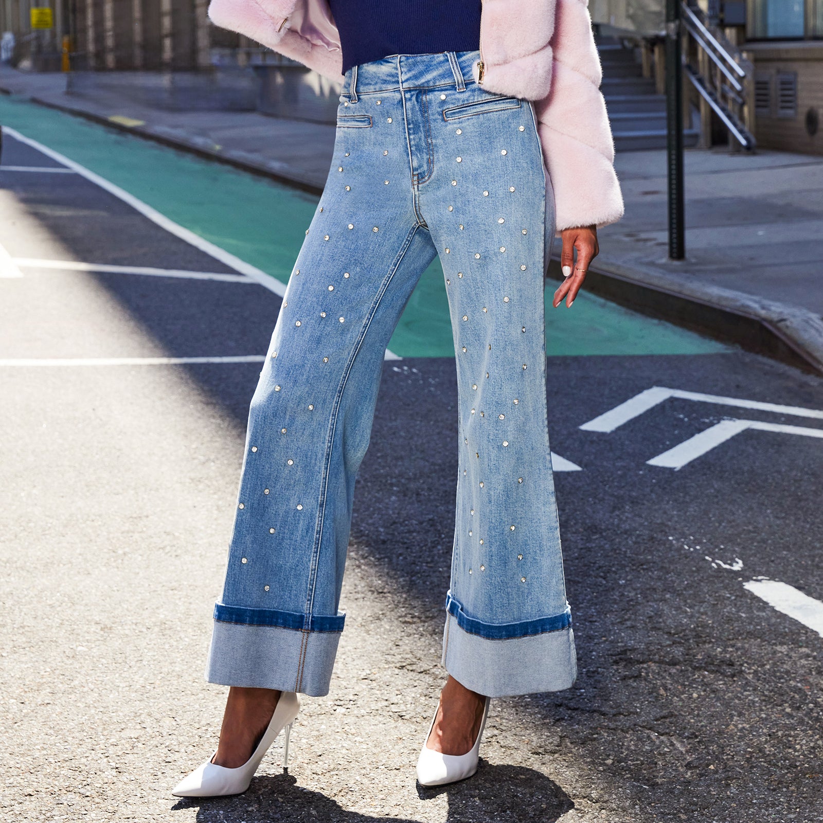 Person wearing blue jeans with crystal embellishment details on a city street.