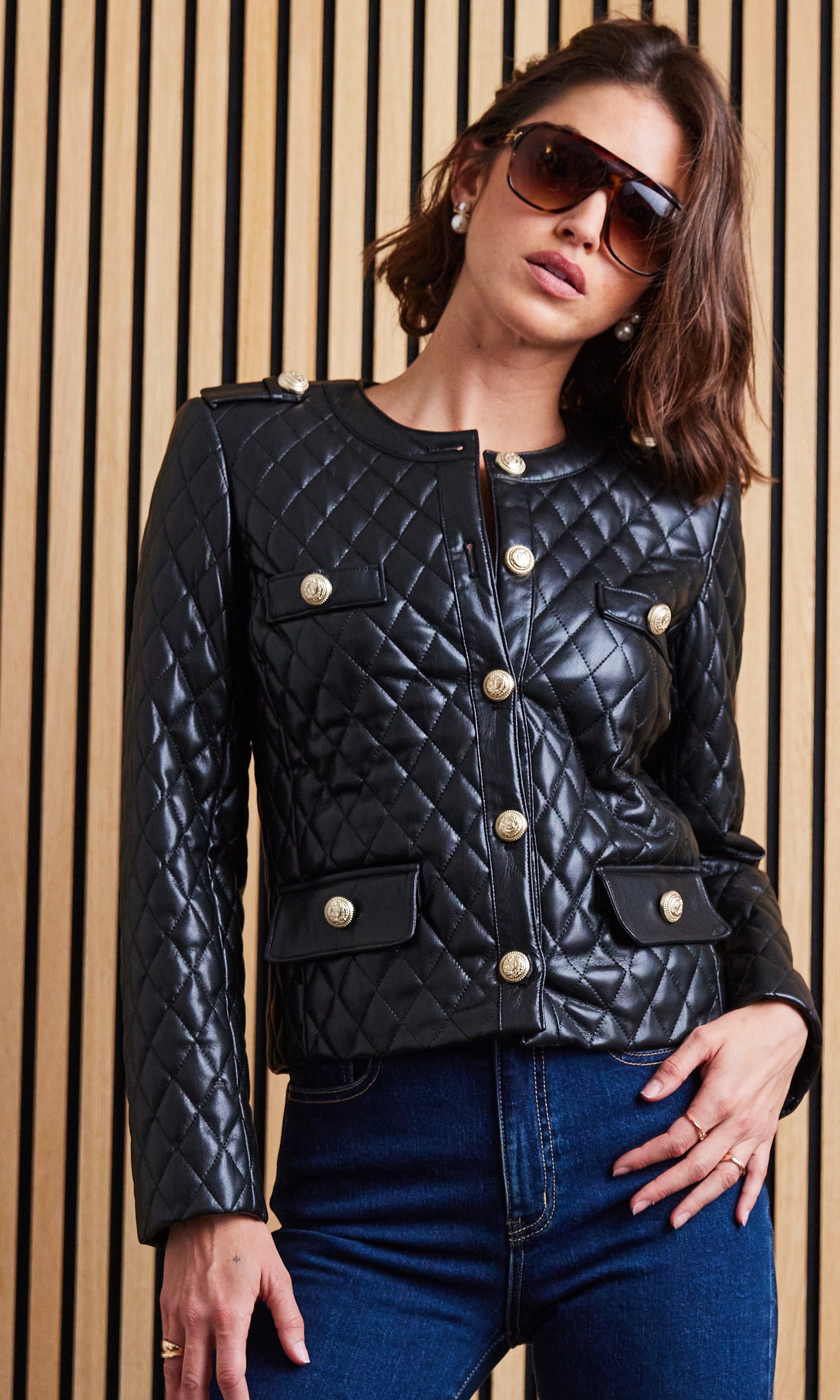 Woman wearing a black quilted jacket with gold buttons against a wooden panel background