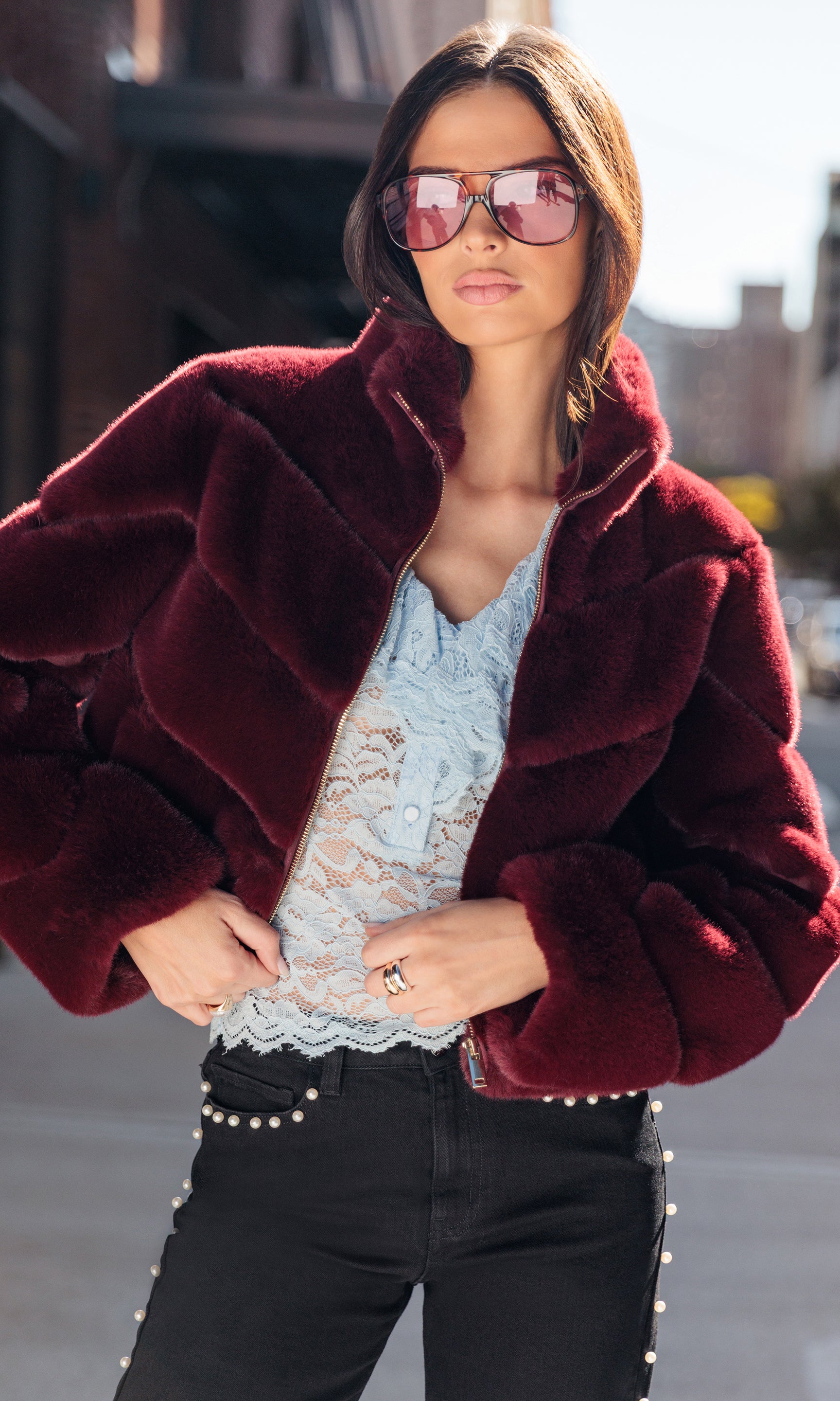Woman wearing a burgundy fur coat, lace top, and black pants outdoors.
