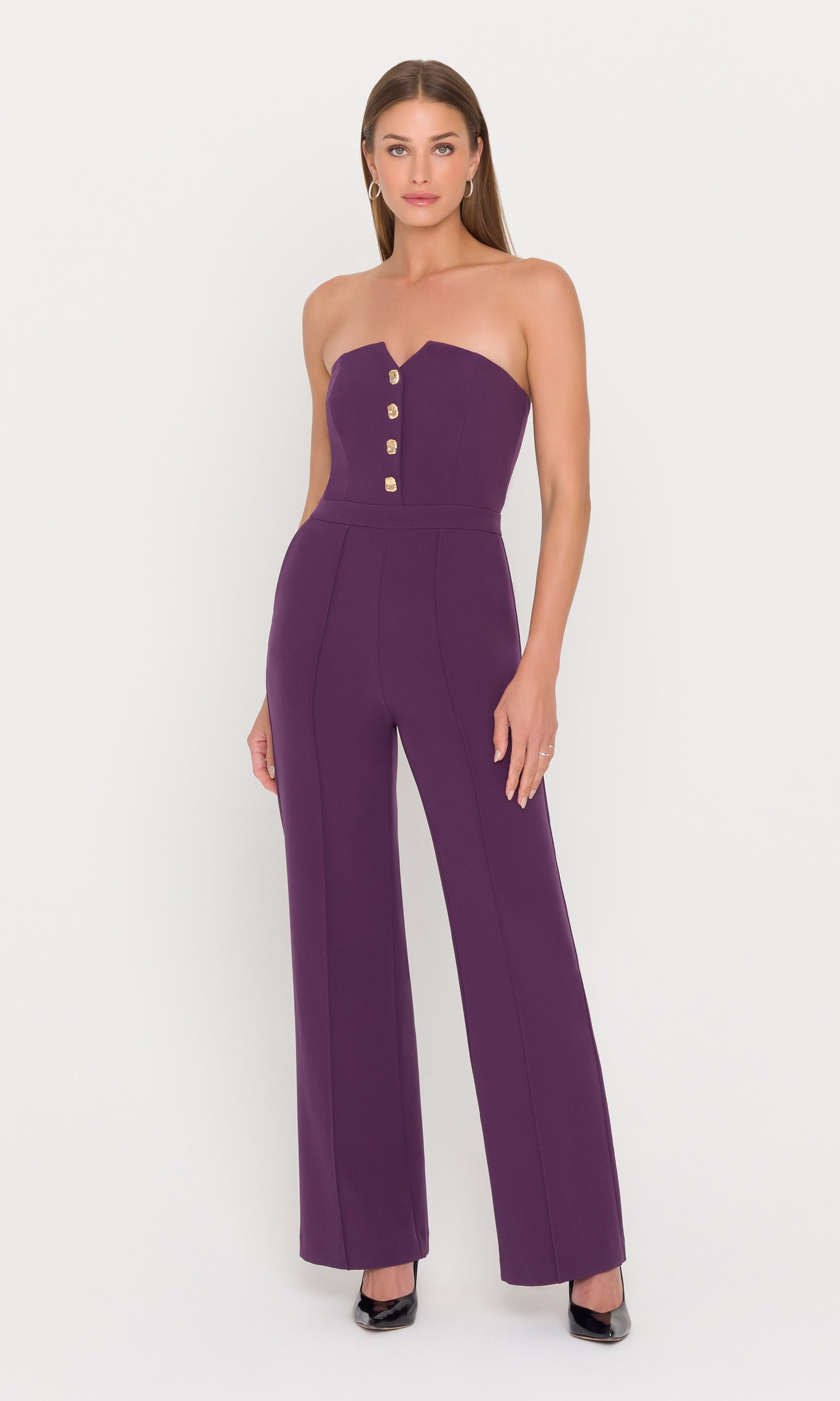 Model wears a strapless eggplant jumpsuit with gold buttons.