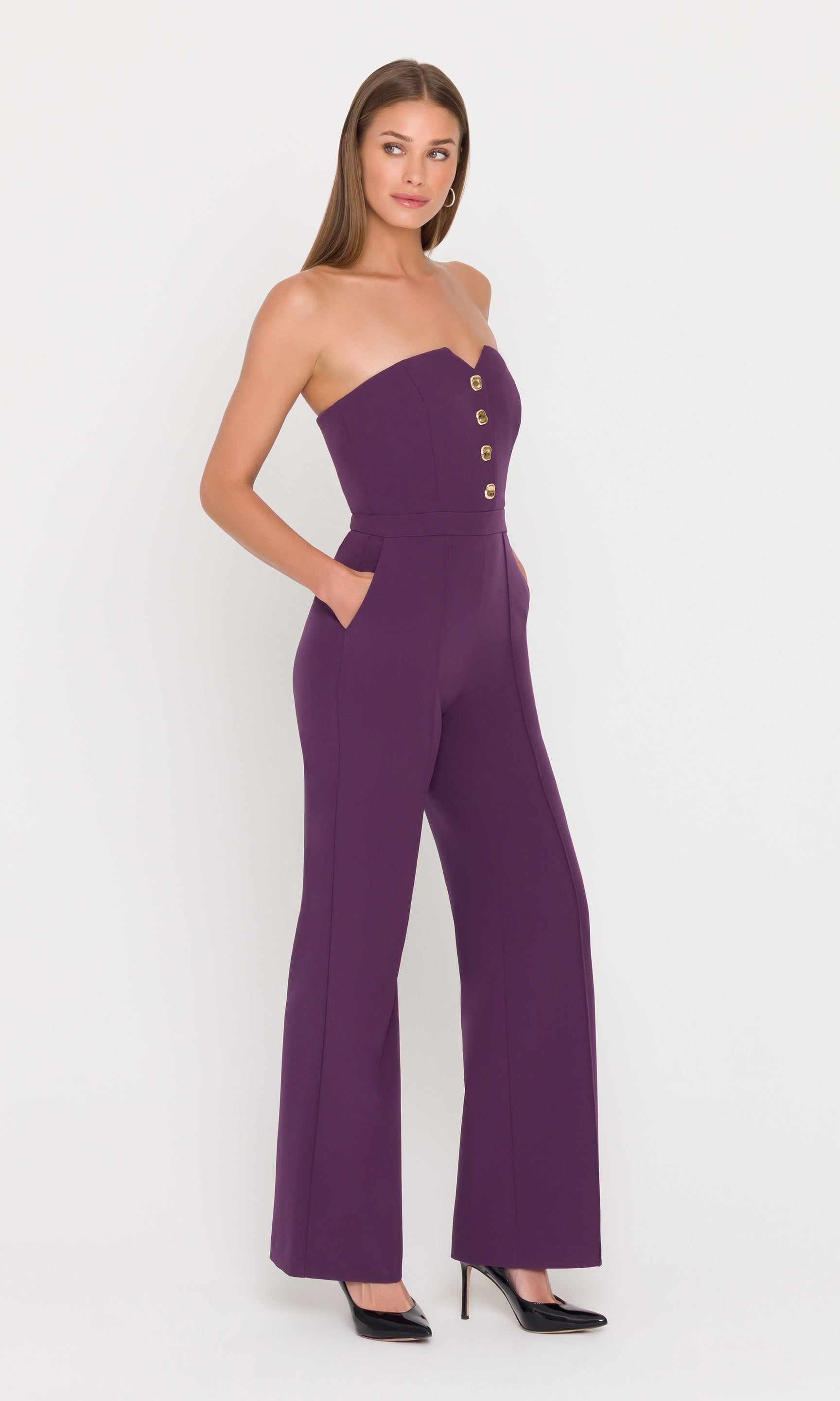 Model wears a strapless eggplant jumpsuit with gold buttons.