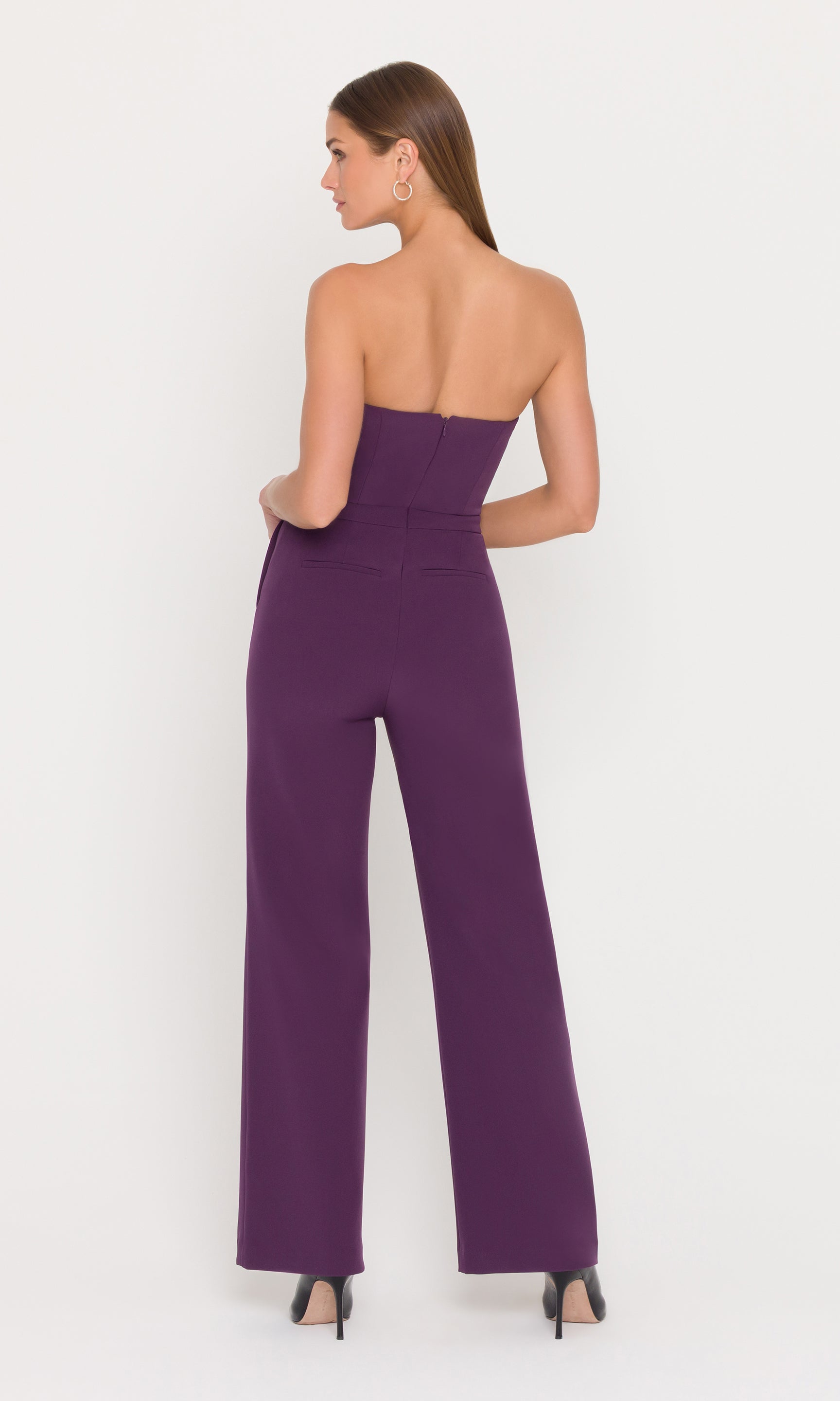 back view of a model wearing a strapless eggplant jumpsuit with gold buttons.