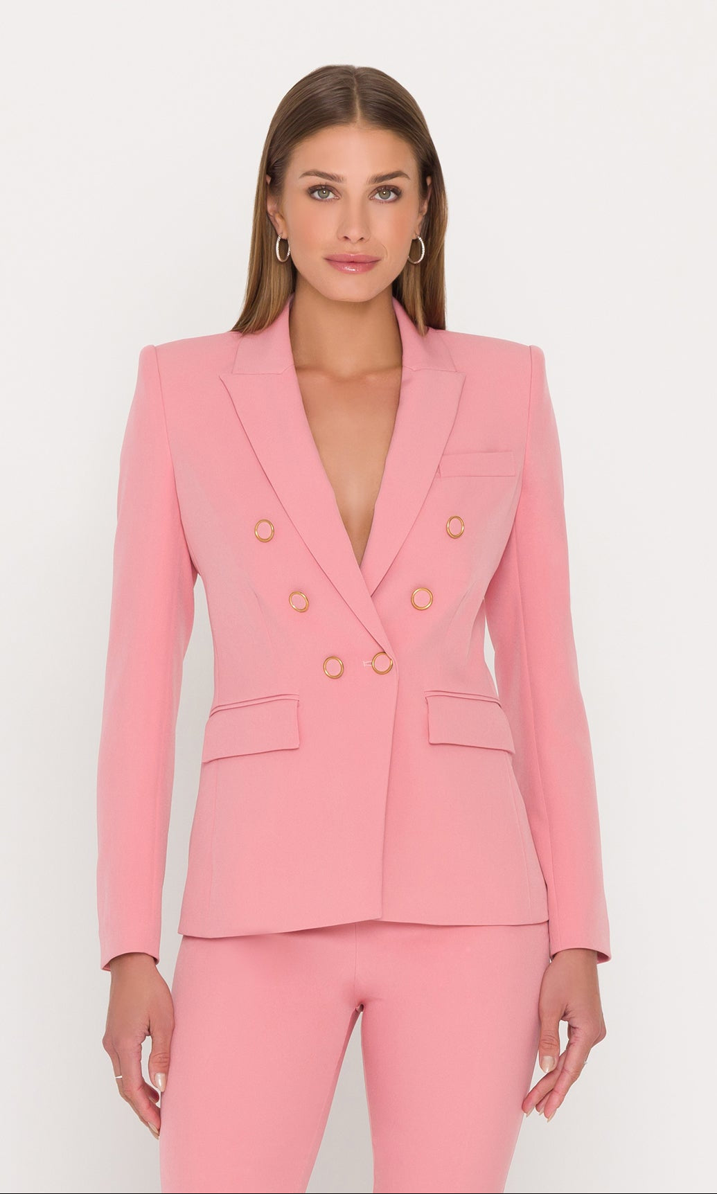 model stands wearing a pink blazer with gold buttons and matching pants