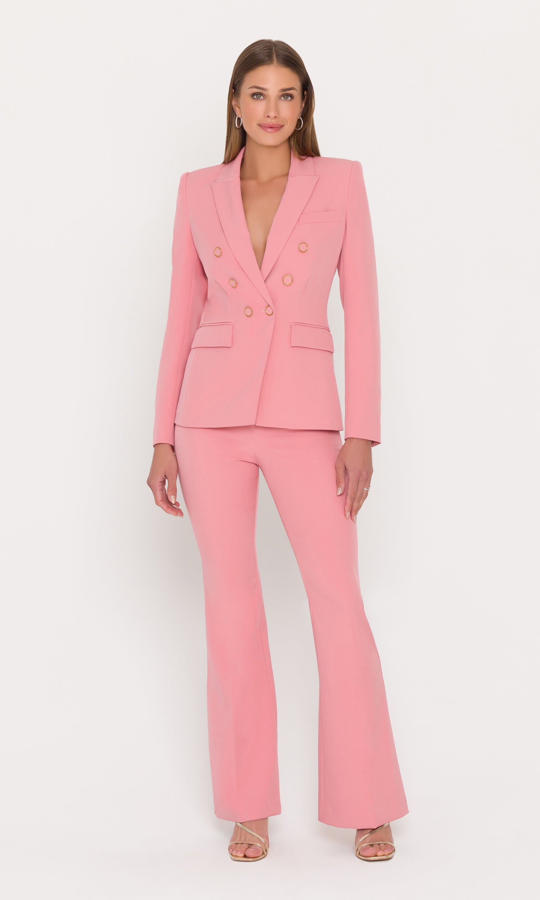 model stands wearing a pink blazer with gold buttons and matching pants