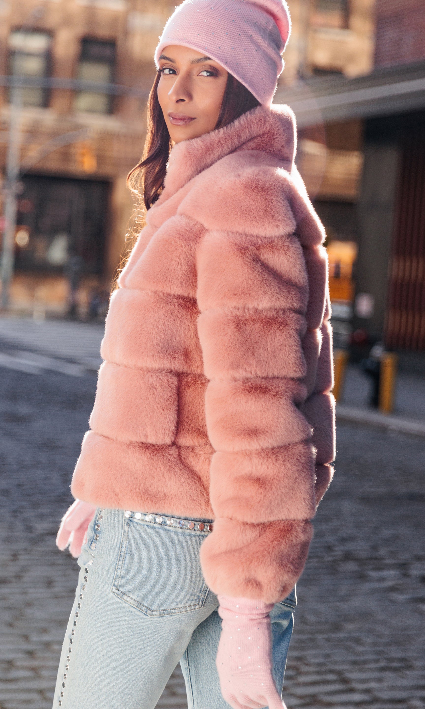 Person wearing a pink fur coat and matching hat on a street.