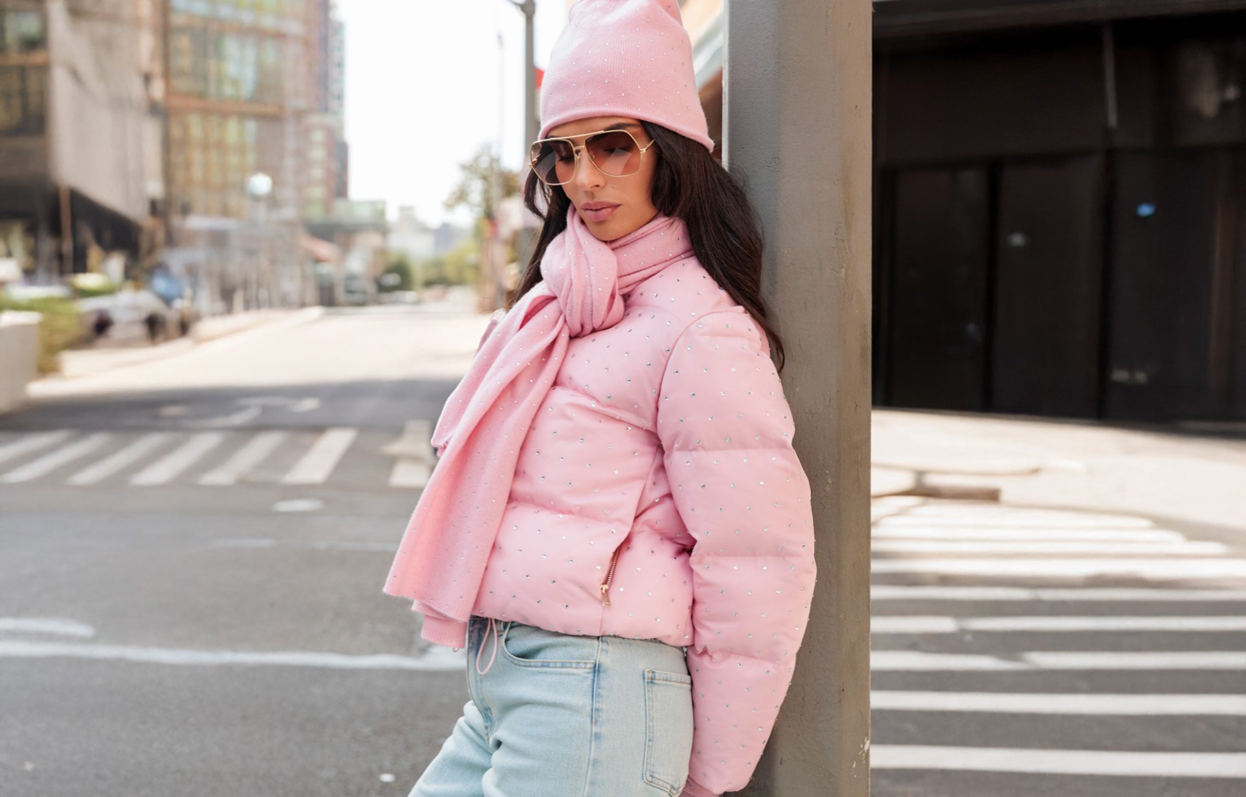 Woman wearing a pink puffer jacket and hat on a city street.