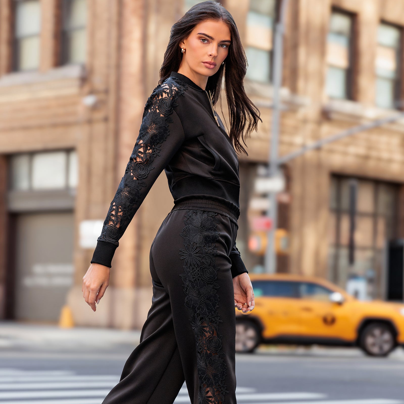 Woman in black lace outfit walking on a city street with a yellow taxi in the background