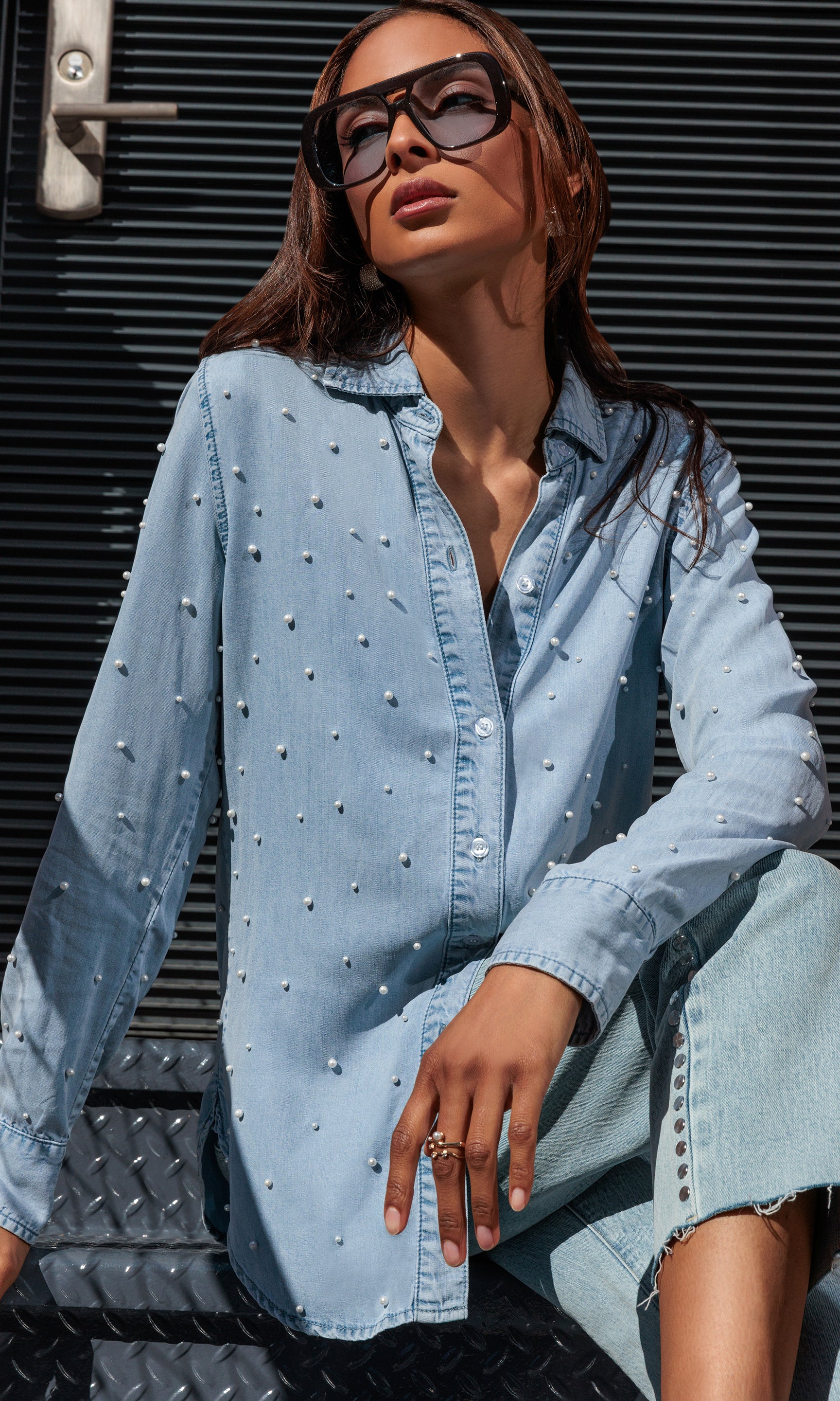 Woman wearing a light blue denim outfit with sunglasses against a dark background