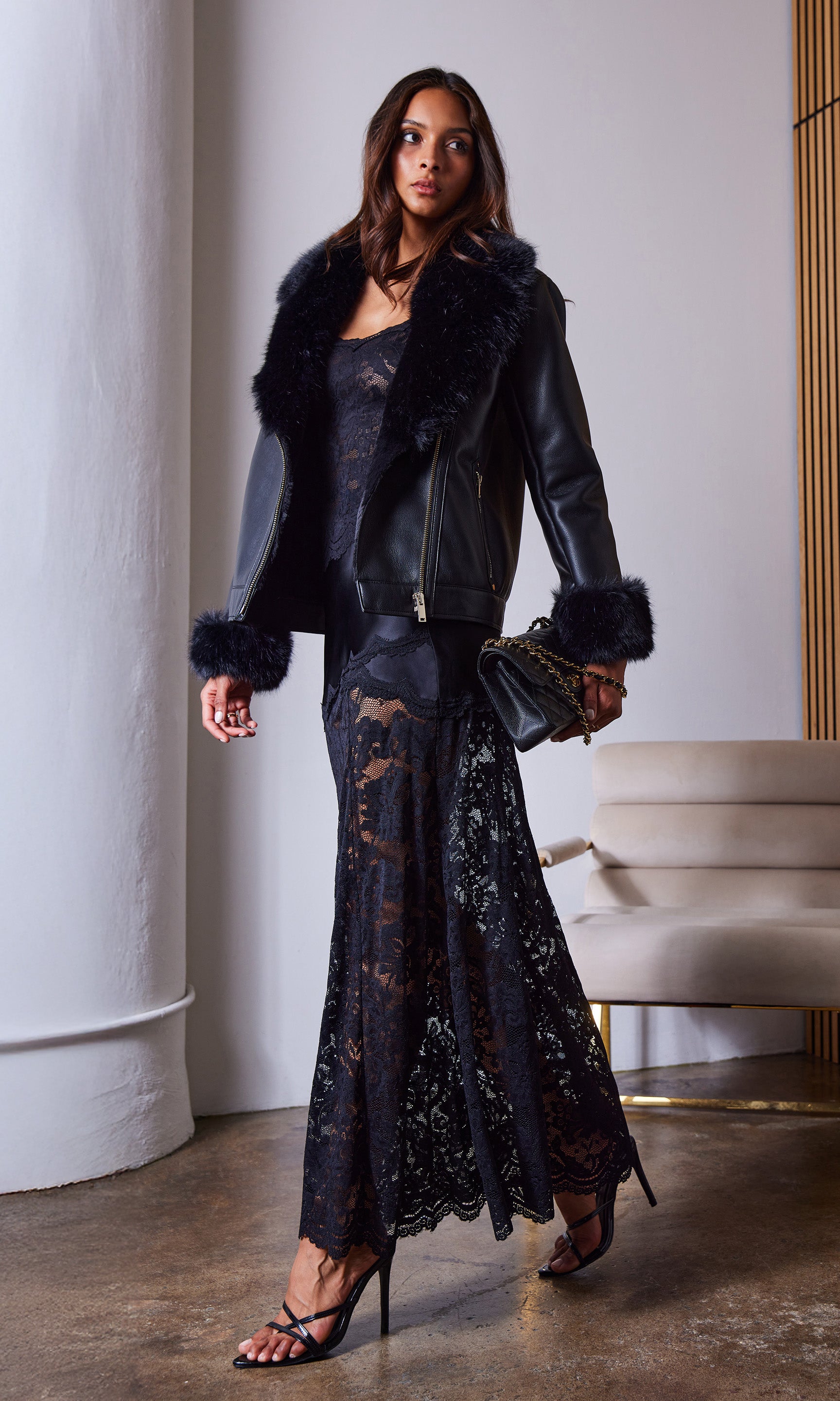 Full body front view of the model wearing the Perrine Lace Combo Satin Skirt paired with a black fur-trimmed jacket and strappy heels, photographed indoors.