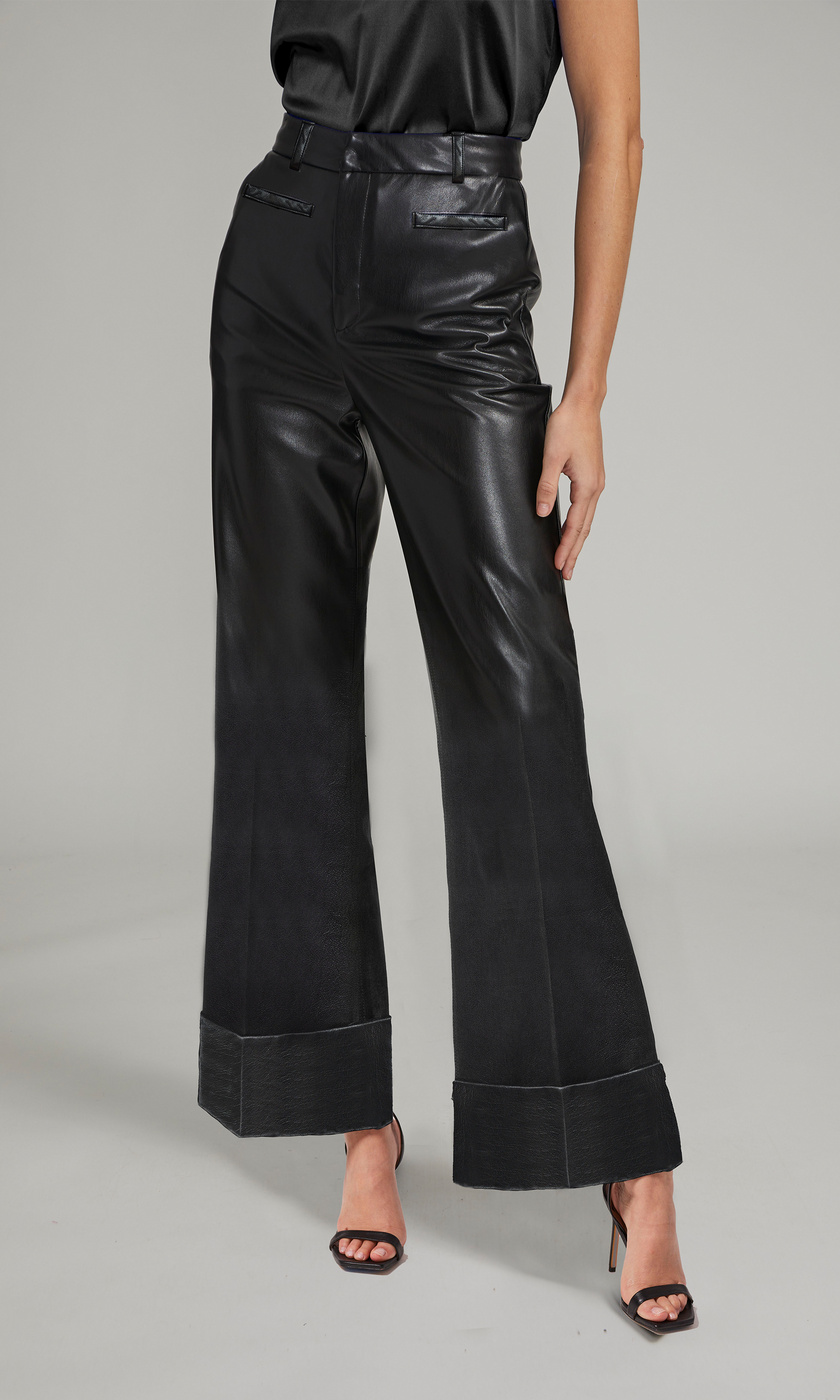 A model showcases stylish black vegan leather pants, highlighting their sleek design and modern appeal.