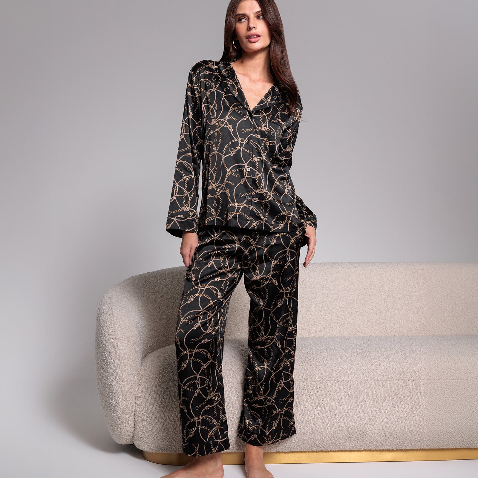 Woman wearing a black patterned pajama set sitting on a beige chair against a gray background