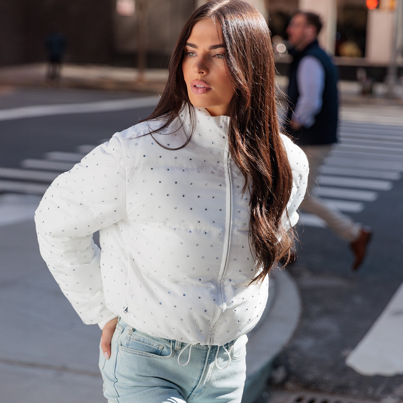 Woman wearing a white crystal embellished jacket and light blue jeans on a city street.