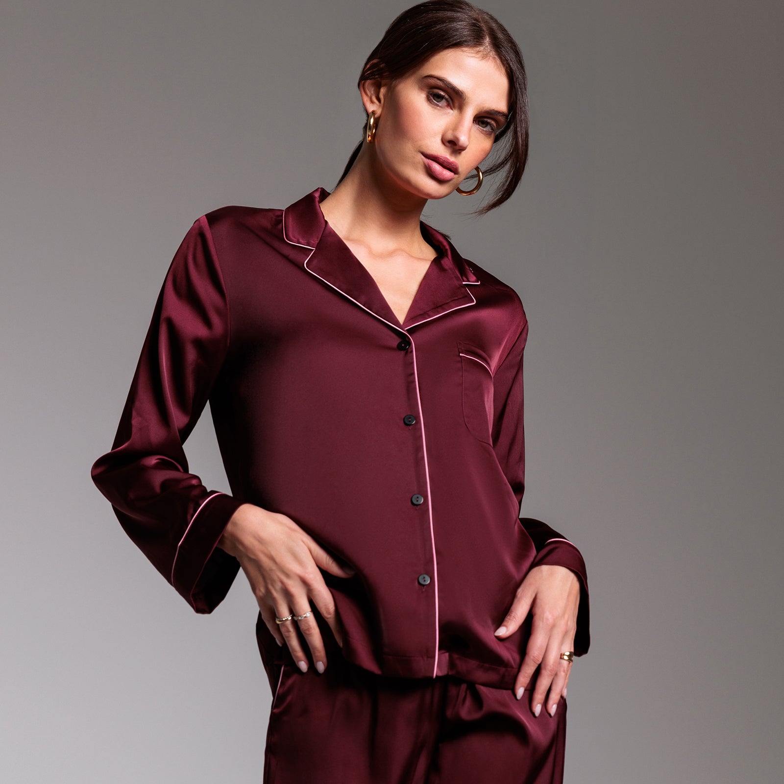 Woman wearing a burgundy satin pajama set against a gray background