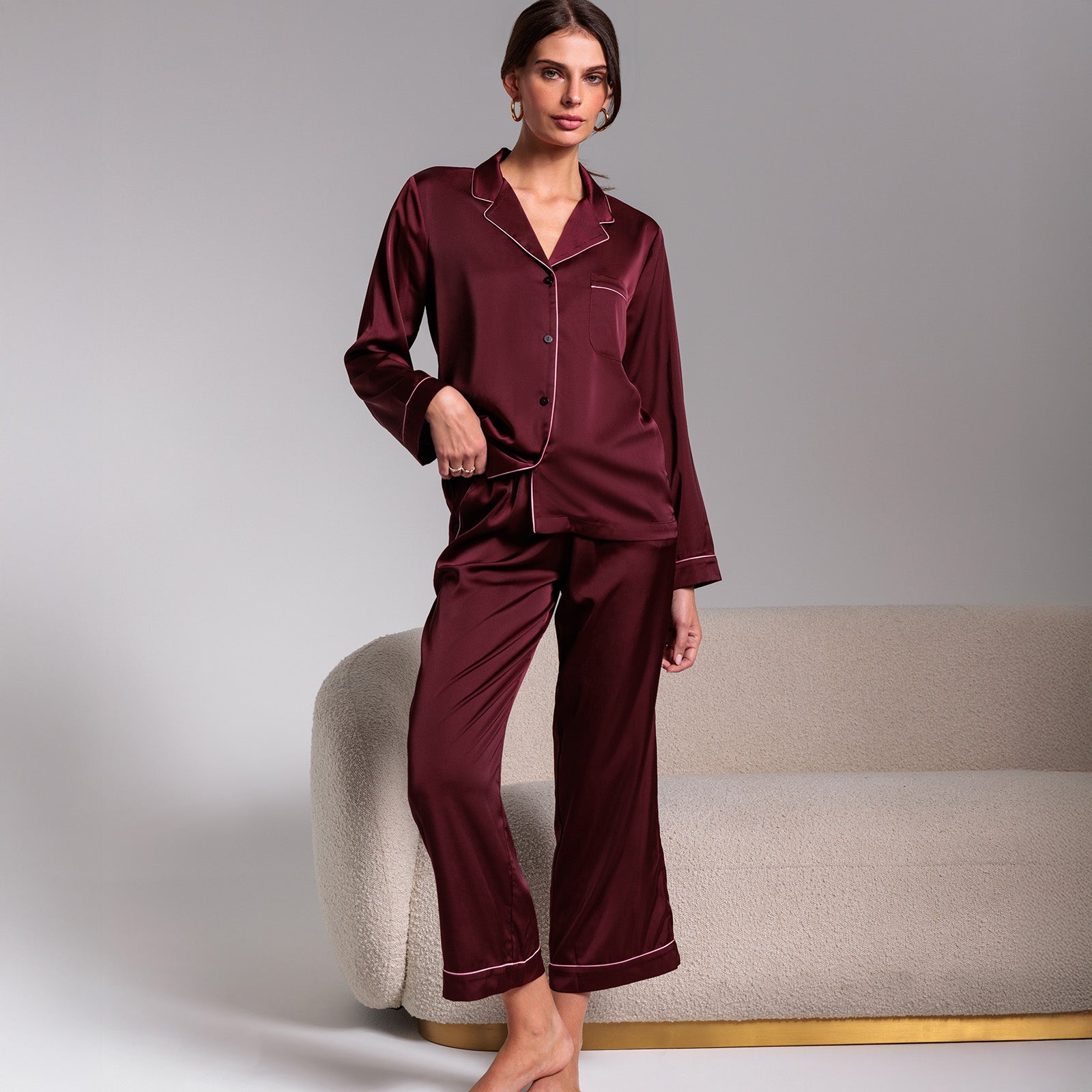 Woman wearing burgundy satin pajamas against a neutral background