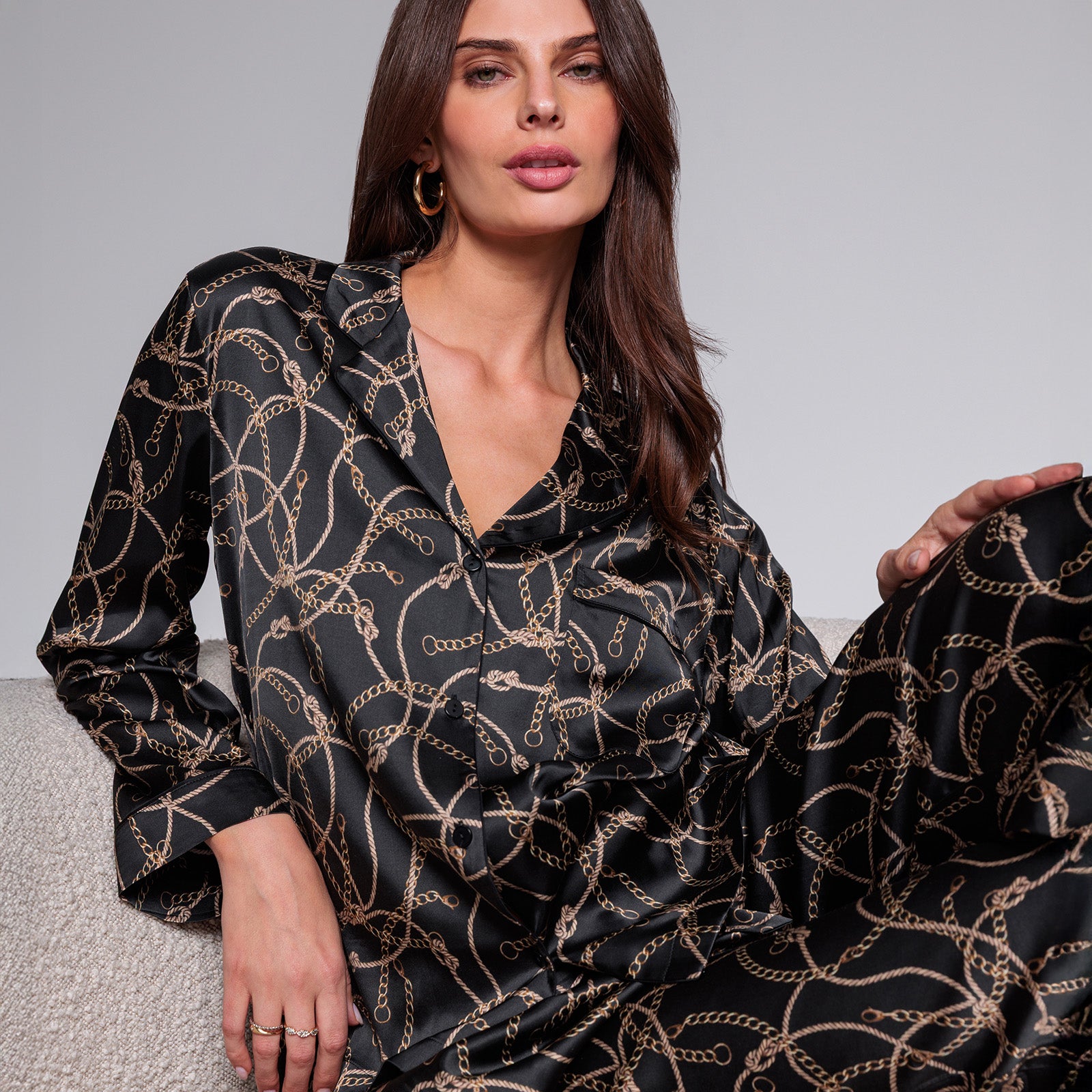 Woman wearing a black blouse with gold chain pattern against a gray background