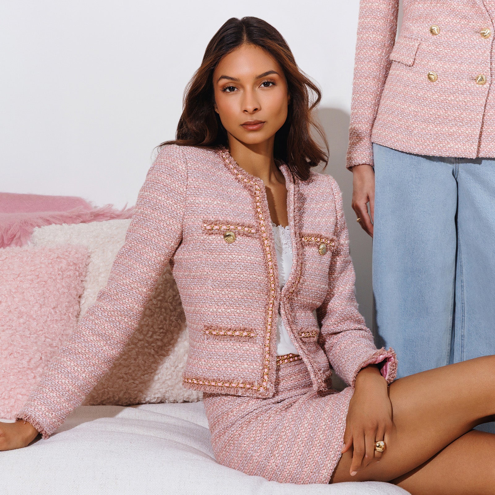 Woman wearing a pink tweed suit sitting on a white surface with a gray background
