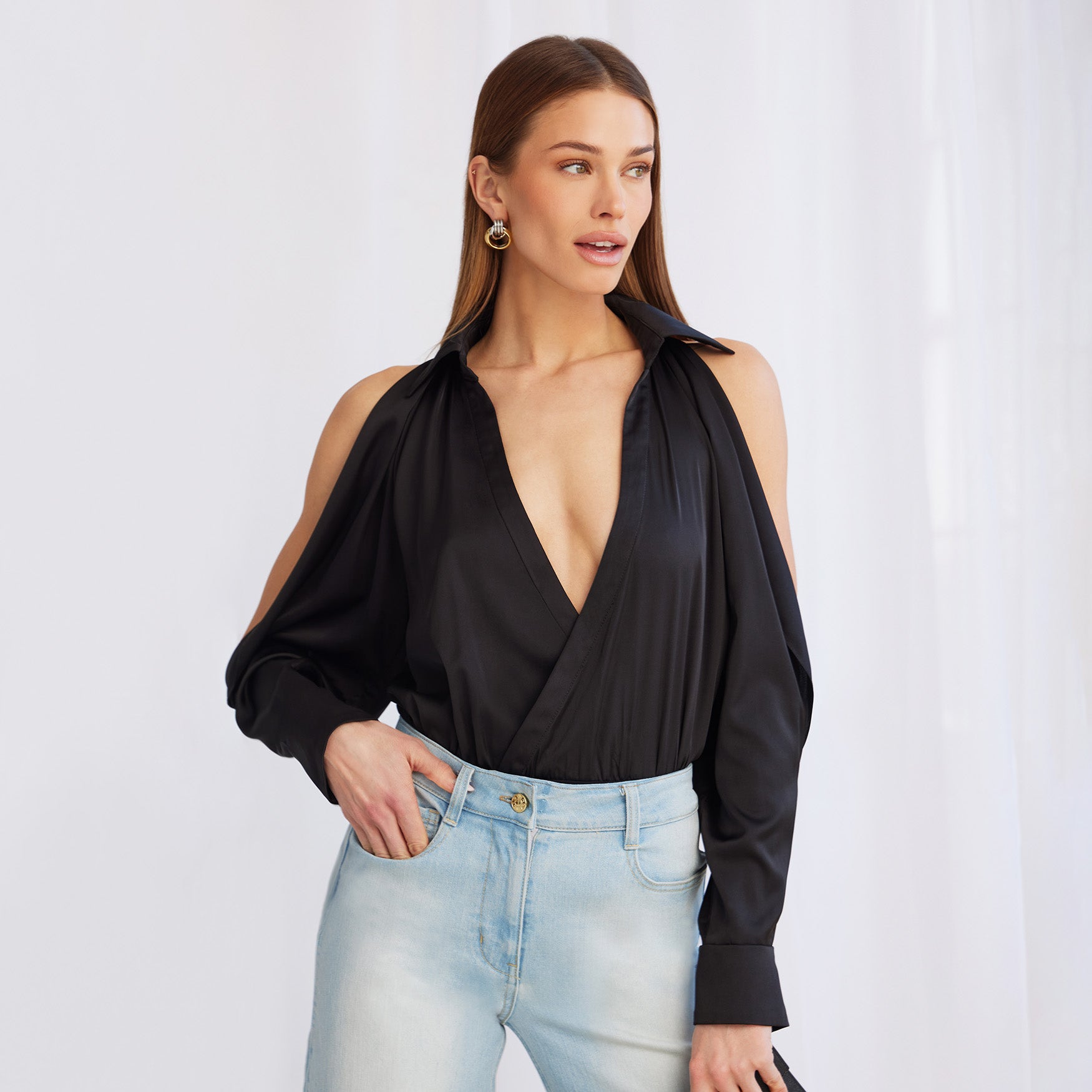 image of model posing in a white room, wearing the Dee bodysuit in black paired with light blue jeans holding a black clutch purse
